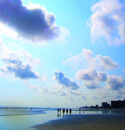 Sky reflection on beach with walkers.